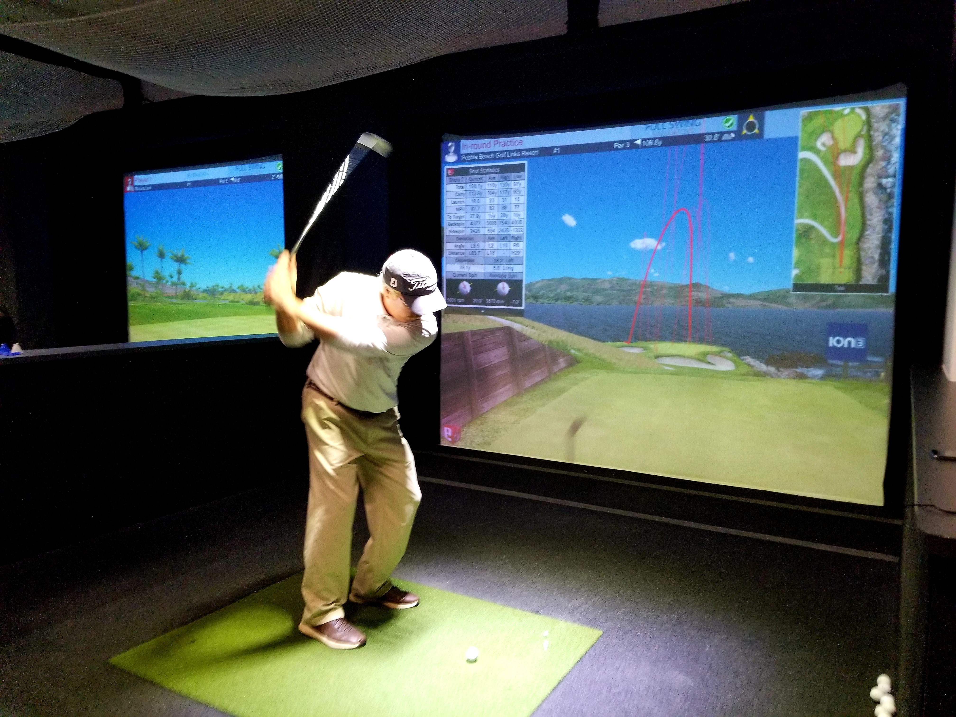 Golfer swings at an indoor simulator bay